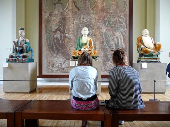 Sitting With by Dorothee Lang -- museum-goers sitting in front of Buddha statues